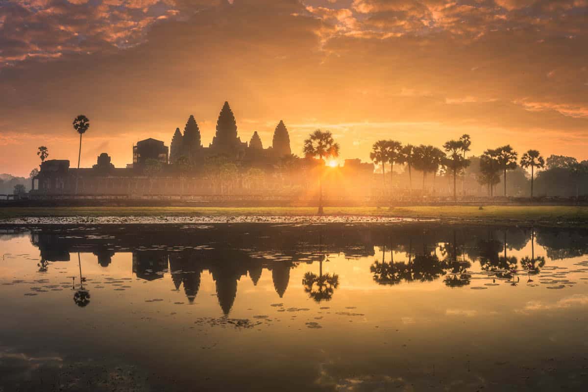 Angkor Wat emerges through golden mist beyond a reflecting pond in Siem Reap, Cambodia.